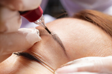 Beauty master performs permanent eyebrow makeup in a beauty salon, microblading, close-up