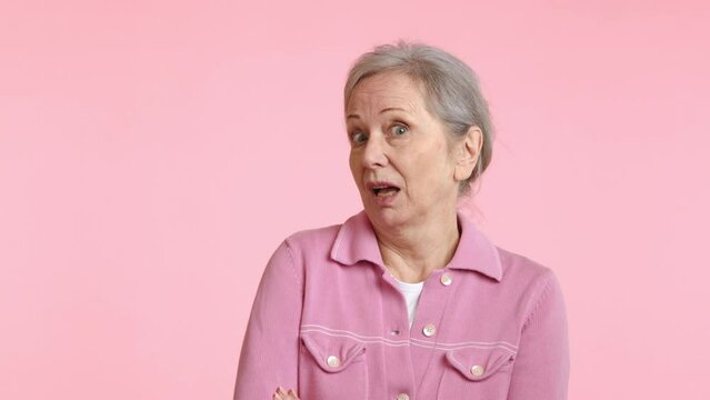 In this scene, a senior woman in a pink jacket displays a sarcastic expression, raising her eyebrows in disbelief and confusion about an unclear situation, with a pastel pink backdrop.