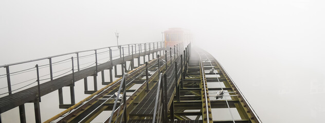 Panorama heritage tram train on lifted aerial electric light rail transit in foggy misty winter...