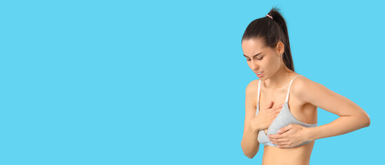 Young woman feeling pain while touching her breast on light blue background with space for text. Cancer awareness concept