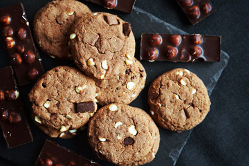 Chocolate cookies next to dark chocolate slices with nuts on a black stand on a dark background