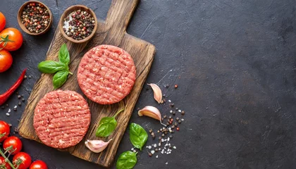 Tuinposter fresh raw hamburger patties or cutlet on brown board ready to cook on black textured background minced beef steak burgers with spices top view place for text © Diann