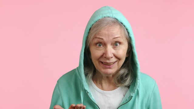 Video captures the delightful moment an elderly woman in a mint hoodie cannot believe her luck, showing overwhelming joy and surprise, with a pink backdrop enhancing her excitement.