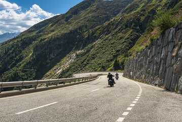 Two bikers riding on the winding Grimsel Pass road, Obergoms, Canton of Valais, Switzerland - obrazy, fototapety, plakaty