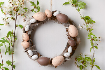 Fototapeta na wymiar Easter wreath made of eggs and feathers with branches hanging on white wall