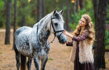 Portrait of beautiful blonde curl girl in medieval dress and fur vest on  nature with horse. Young...