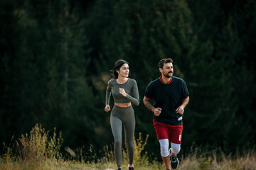 Fototapeta premium Active couple running together in the mountain wilderness, surrounded by tall pine trees