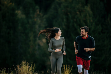 Fit couple jogging amidst a scenic mountain landscape, dressed in sporty attire