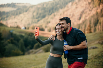 Multicultural pair in workout attire taking a breather, staying hydrated, and using smartphone for a selfie