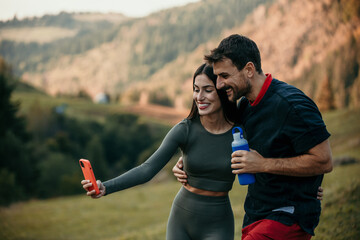 Fitness enthusiasts, a woman, and a man, relaxing after a jog, drinking water, and browsing their...