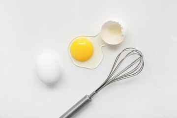Cracked and whole chicken eggs with whisk on white background