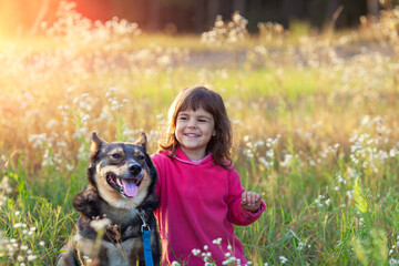 Naklejka na ściany i meble Happy Little girl with a dog walking in the flower field in spring