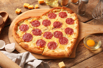 Board with tasty heart shaped pizza and ingredients on wooden background