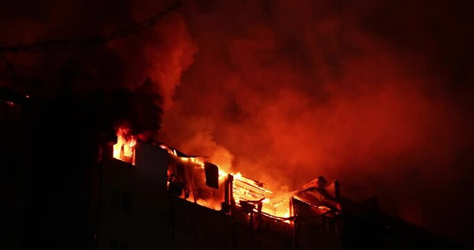 Huge fire blazing in apartment building. Burning house is engulfed in flames at night during the disastrous