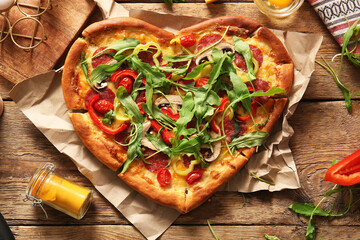 Tasty heart shaped pizza with arugula on wooden background