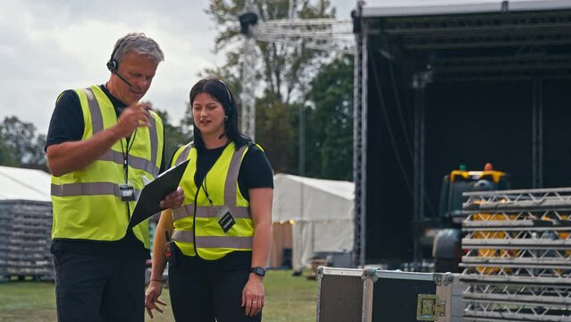 Production Team With Headsets And Clipboard Setting Up Outdoor Stage For Music Festival Or Concert