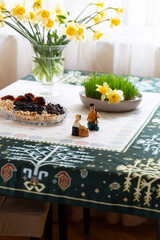 Novruz traditional wheat grass semeni or sabzi, in a plate with sweets and dry fruits and yellow daffodils on ethnic pattern white and green table cloth, spring equinox celebration in Azerbaijan