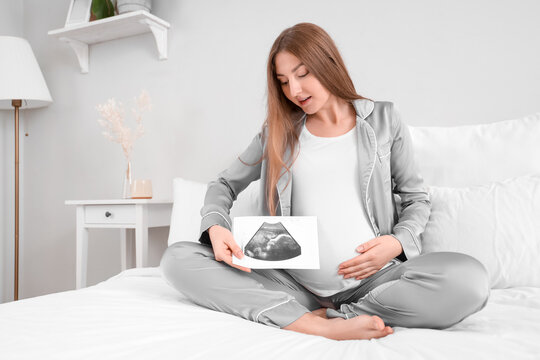 Young pregnant woman with sonogram image sitting in bedroom