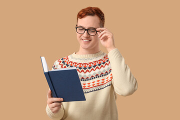 Young man in eyeglasses reading book on color background