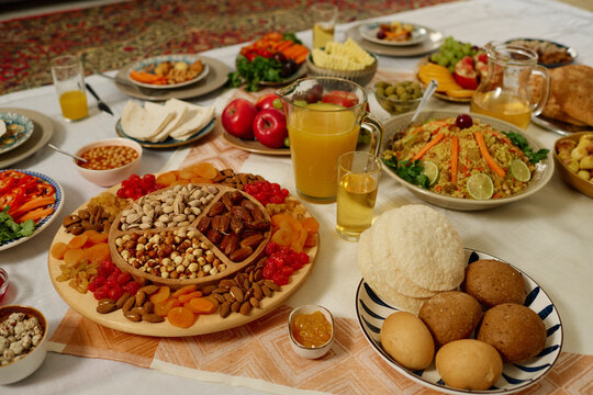 Tablecloth on the floor with appetizing homemade bread, jug and glass with juice, pilaf, dried fruits and other food prepared for dinner