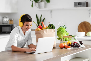 Cute little boy with different vegetables and modern laptop in kitchen