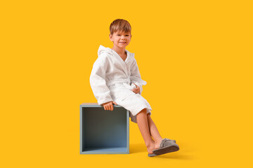 Cute little boy in bathrobe sitting on yellow background