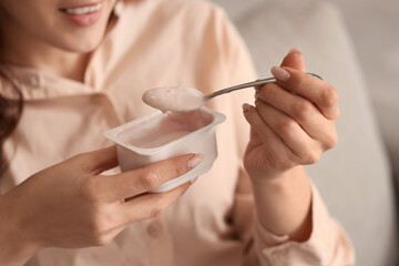 Young woman eating tasty yoghurt at home, closeup
