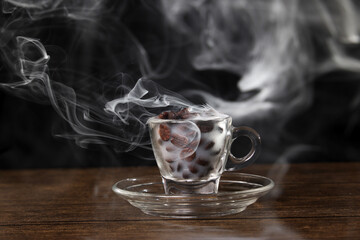 Smoke vape fog flowing out of transparent glass coffee cup filled with coffee beans on dark black background