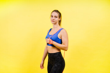 Portrait of gentle muscular woman holding skipping rope on her neck isolated over yellow background