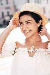 Young beautiful smiling hipster woman in trendy summer costume clothes. Carefree female posing in the street at sunny day. Positive model outdoors at sunset. Cheerful and happy in hat