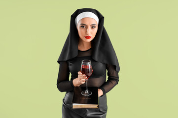 Sexy nun with glass of wine and Holy Bible on green background