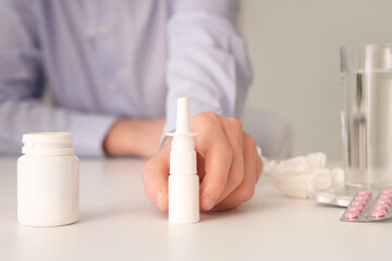 Ill businessman with nasal drops and pills on table in office, closeup