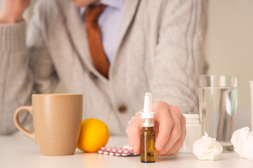 Ill businessman with nasal drops, lemon and pills on table in office, closeup