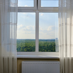 Window with curtains overlooking the forest and the sky in the clouds
