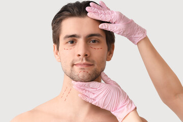 Plastic surgeon and young man with marked face on light background, closeup