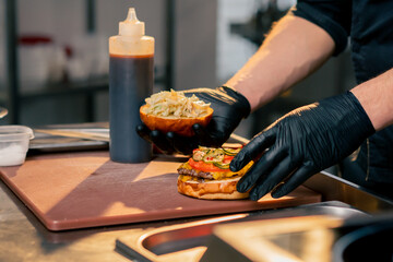 close-up of chef's hands in the kitchen of the establishment covering the finished burger with one...