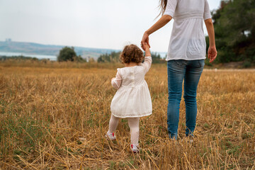 Mother little child holding hands walking in a grass field.Stock photo . - 736103375