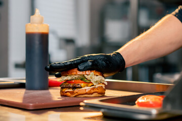 close-up of the hands of a chef in the kitchen of a restaurant attaching one half of a bun to the...