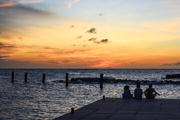 Obraz premium People sitting on the jetty during sun setting in Caribbean sea.