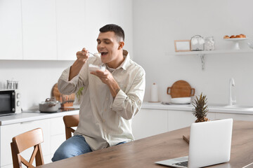 Young man eating tasty yogurt in kitchen - Powered by Adobe