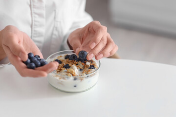 Young woman with blueberries and tasty yoghurt at table in kitchen, closeup