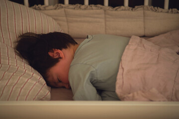Baby boy sleeps in a crib and tosses, kid age two years and five months. The child is sleeping in bed