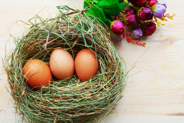 Three raw eggs in the hay nest and bouquet of flowers on wooden table. Easter concept