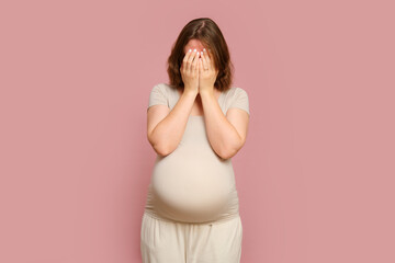 A crying pregnant woman on a pink studio background. Pregnancy of an unhappy woman with a belly