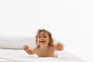 Obraz na płótnie Canvas Adorable baby, little girl with wet hair lying in diaper on bed, embodying innocence and joy against white background. Concept of childhood, motherhood, life, birth. Copy space for ad