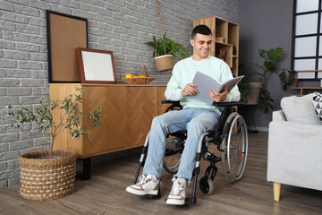 Happy young man in wheelchair reading magazine at home