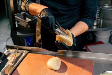 A quick shot of a chef wearing black gloves using tongs to open bun before adding the ingredients