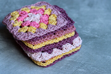 Handmade crocheted zigzag ornaments on grey background with copy space. Colorful cotton granny square. Crochet texture close up photo. 