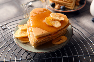Plate with tasty pancakes in shape of heart and dried banana on grey tile background, closeup....