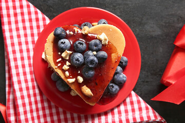 Plate with tasty pancakes in shape of heart, blueberry and jam on dark background, closeup. Valentine's Day celebration